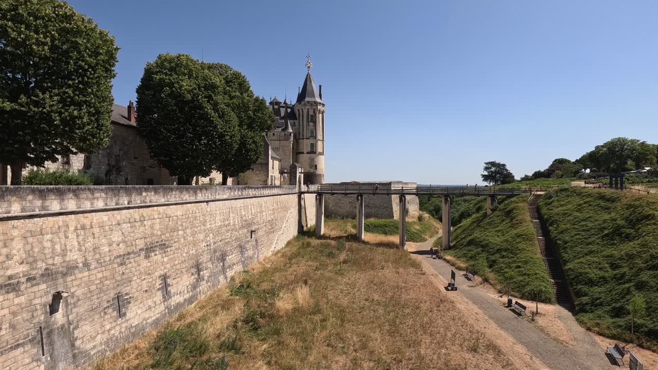 Walking path traverses old dry moat, bridge to Saumur Castle in Loire