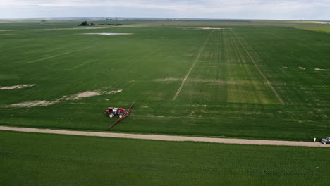 Tractor-Agrícola-Rociando-Pesticidas-En-El-Campo-De-Trigo-Verde-En-El-Campo-En-Saskatchewan,-Canadá---Drone-Aéreo