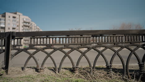 close view of an intricate metal fence with a weathered look, showcasing detailed patterns, with cars passing by