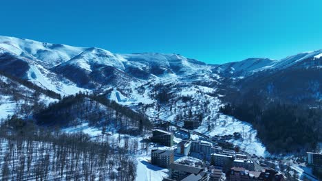 계곡에 자리잡은 눈으로 인 산악 마을의 공중 풍경, 매력적인 집과 주변의 눈 인 봉우리, 아한 겨울 풍경을 만니다.