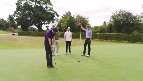 Male golf players wearing uniforms, playing golf and knocking golf ball into cup on golf course