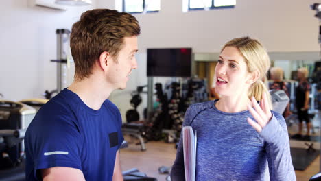 man exercising on cycling machine being encouraged by personal trainer in gym