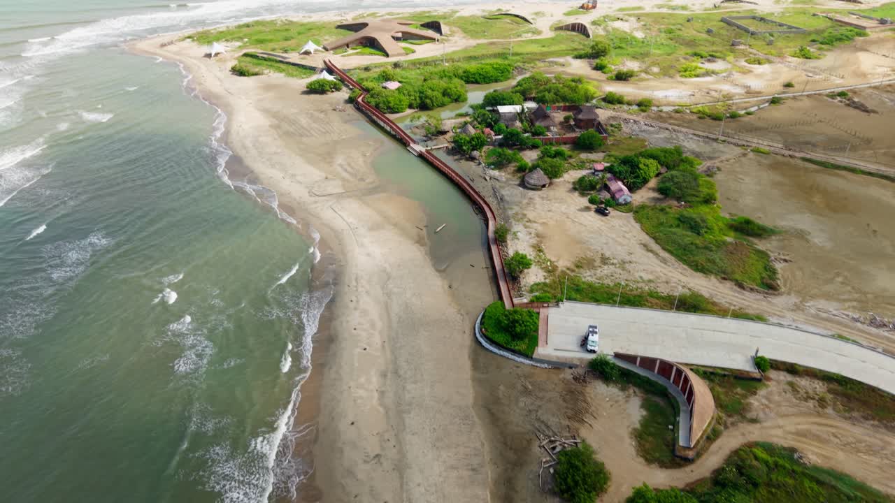 Aerial view of a coastal road traversing a beach, alongside lush vegetation and the vast expanse of the atlantic ocean in salinas del rey, colombia