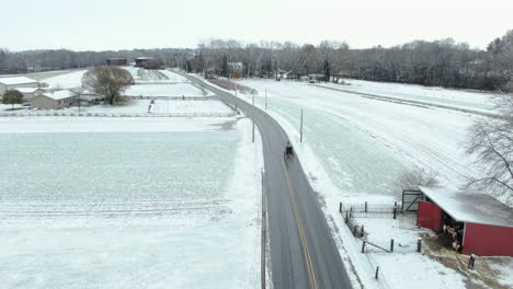 Pennsylvania-countryside-covered-in-thin-layer-of-first-seasonal-snow,-a-horse-carriage-on-empty-road-passing-by-wooden-shed-in-bright-red-color