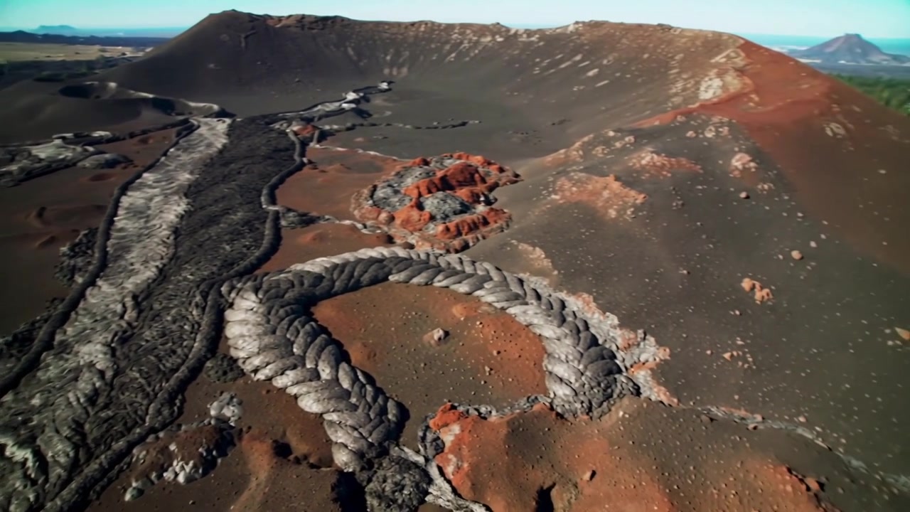 Drone in panoramica che rivela lava intrecciata che avanza, formando cordoni su una piana di cenere, mentre si raffredda.