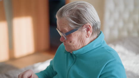lonely pensioner in green teal sweater, adjusting glasses. close-up of elderly woman with wrinkled hands, focused expression, sitting in a calm indoor setting. depicts aging and delicate movements