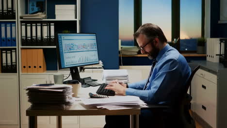 man working late in office with stacks of documents and computer data