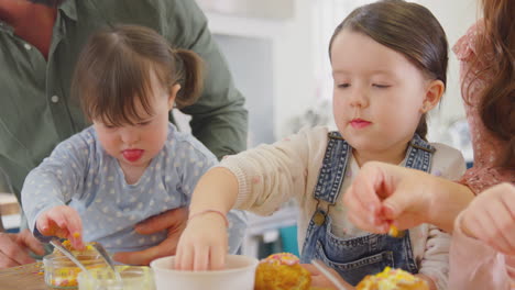 Familie-Mit-Down-Syndrom-Tochter-Backt-Und-Dekoriert-Kuchen-Und-Sitzt-Zu-Hause-Am-Tisch