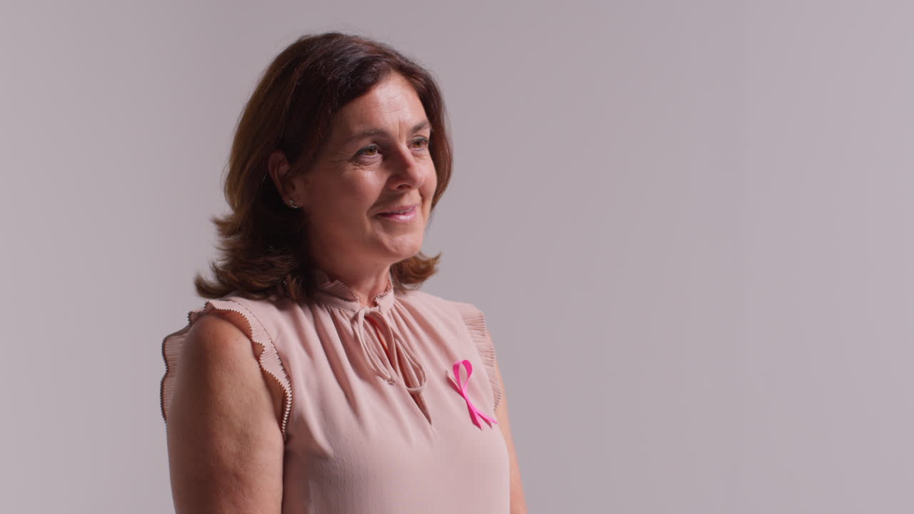 retrato de estudio de mujeres maduras sonrientes que llevan una cinta rosa de concienciación sobre el cáncer de mama contra un fondo blanco