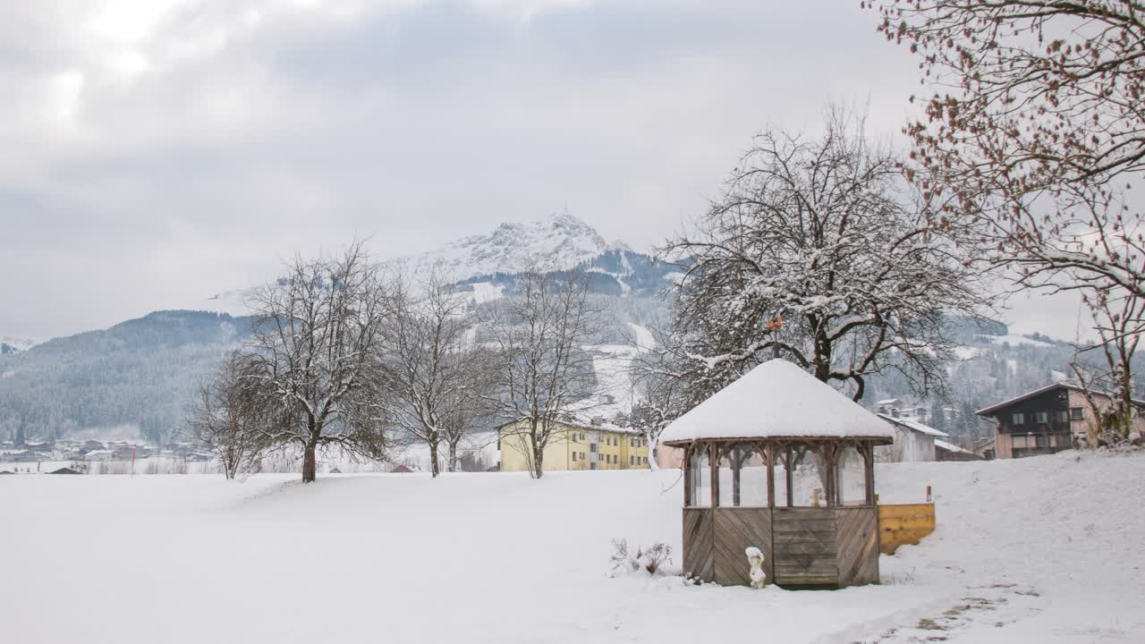 전경에 오두막과 나무가 있는 눈으로 덮인 산 위로 움직이는 구름의 시간 경과