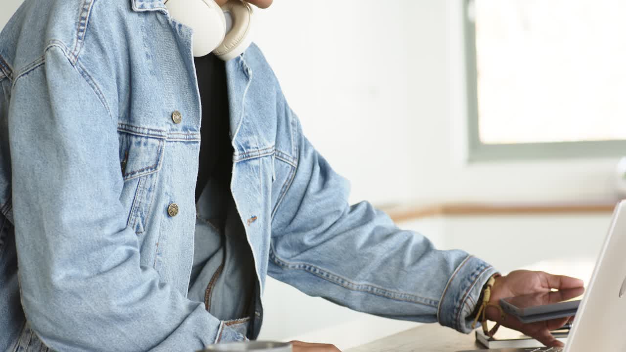 Ein afroamerikanischer Mann mittleren Alters betrachtet sein Telefon am Schreibtisch, legt es neben den Laptop und tippt für die Arbeit.
