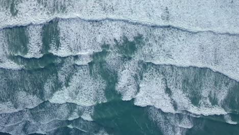 rhythmic and symmetrical foamy waves drift towards shore. mesmerising cinematic top down aerial view