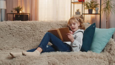 young small teenager girl reading favorite storybook at home sofa quiet smiles tiny serious sighs