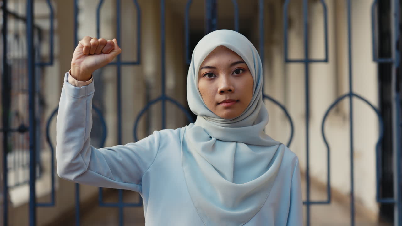 A woman in a hijab raises her fist in a gesture of solidarity or protest