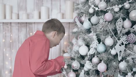 son in red shirt examines silver toys on christmas tree