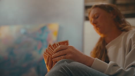 woman sitting fireside holding red hand of cards reaches to draw another, wide handheld 4k