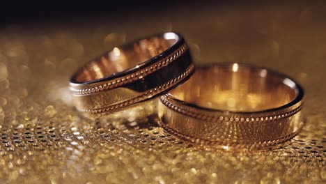 wedding rings lying, rotate, spinning on shiny golden shining surface with light, close-up macro