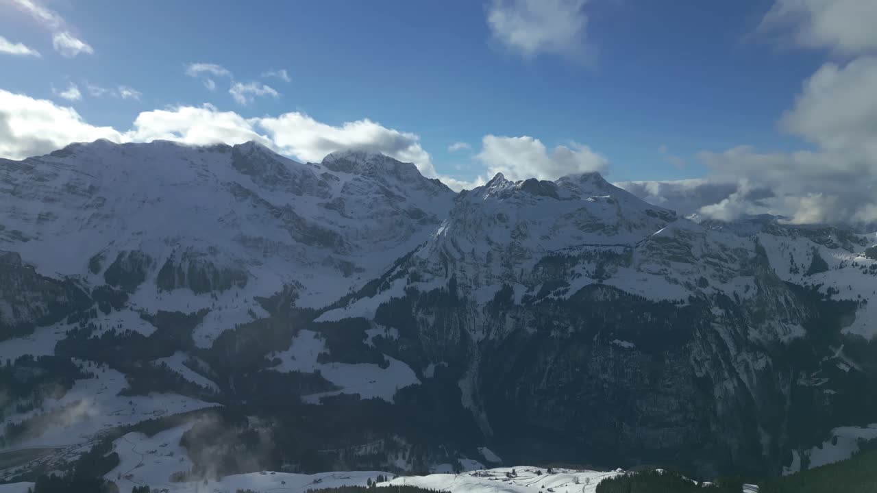 寒い冬の日にスイスのスイスアルプスにあるエンゲルベルク・ブルンニバーネンで、雪に覆われた谷と山脈の上を空撮ドローンがティルトダウンするショット