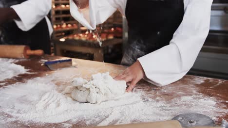 Diverse-bakers-working-in-bakery-kitchen,-kneading-dough-on-counter-in-slow-motion