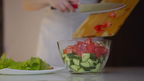 el chef femenino vierte tomates cortados en el cuenco para cocinar ensalada