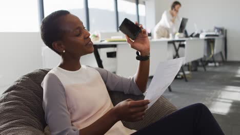 Mujer-De-Negocios-Afroamericana-Trabajando-En-Un-Sillón-Mientras-Su-Compañero-De-Trabajo-Tiene-Una-Llamada-De-Negocios