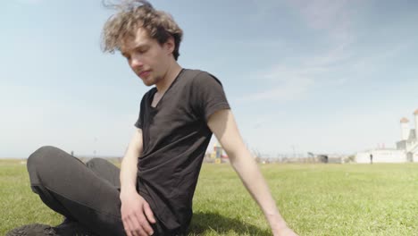 a young male wearing black sits on grass and does stretching exercises