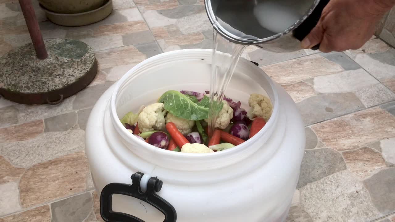 Top view of homemade pickling raw vegetables in brine salt water poured in white plastic barrel container