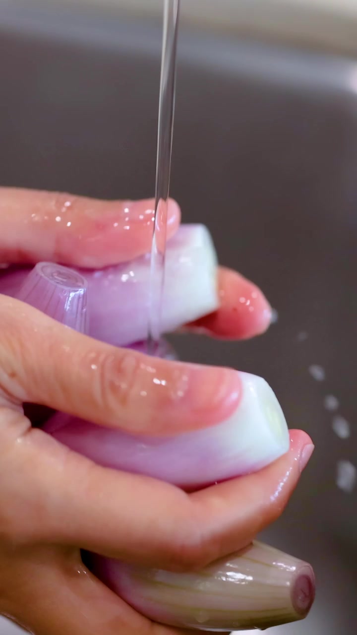 Primo piano di mani che sciacquano scalogni sotto un getto d'acqua in un ambiente di cucina.