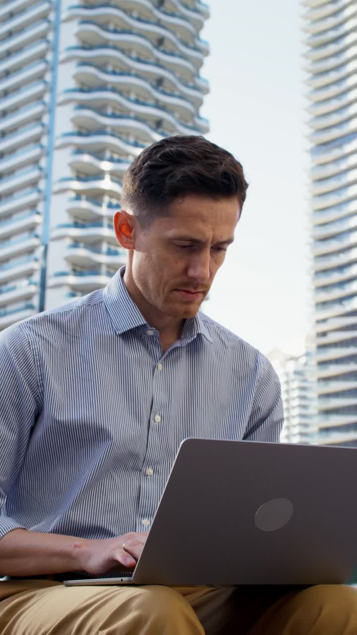 Man working on a laptop in front of skyscrapers.