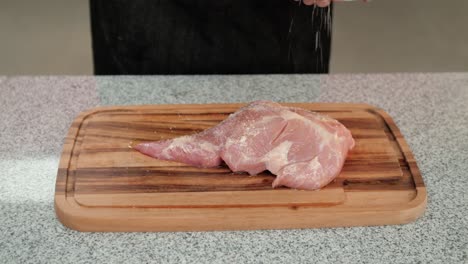 primer plano de un chef agregando sal a una carne de cerdo cruda