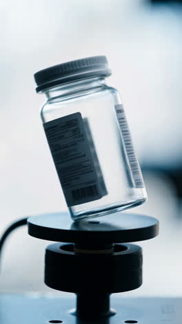 a clear glass medical bottle with a white cap on a testing device