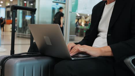 Businessman Uses Laptop, Waiting for a Flight in Airport Terminal or train station, Traveling Entrepreneur Working Online On Computer Sitting in a Boarding Lounge of Airline Hub with Airplanes
