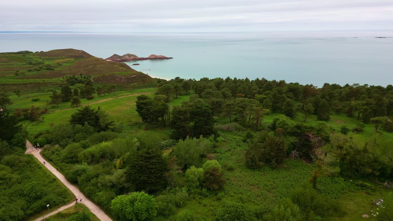 Aerial drone view of a scenic coastal path through lush green landscape at Cap d'Erquy, with the sea in the background, Brittany, France