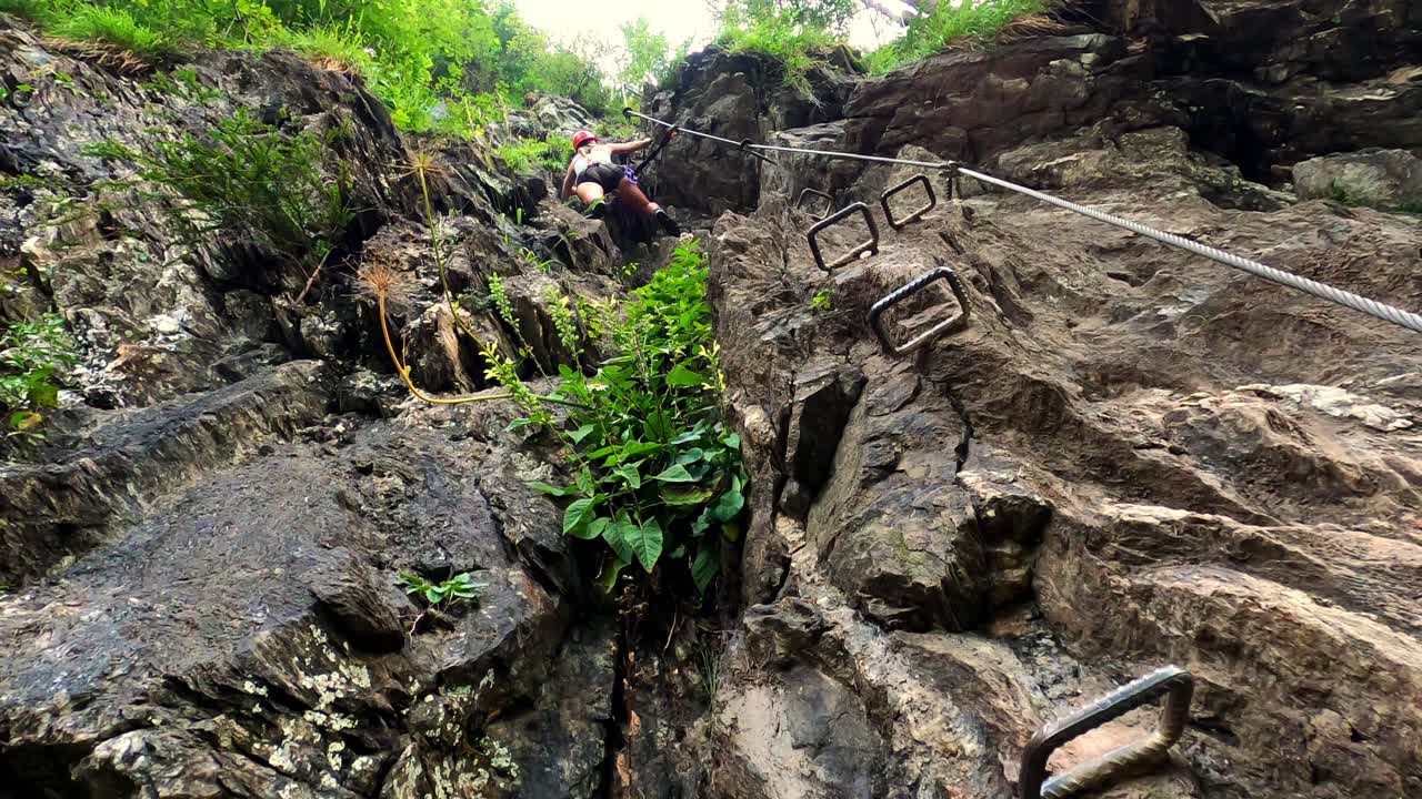 una chica con pantalones cortos negros está subiendo una roca