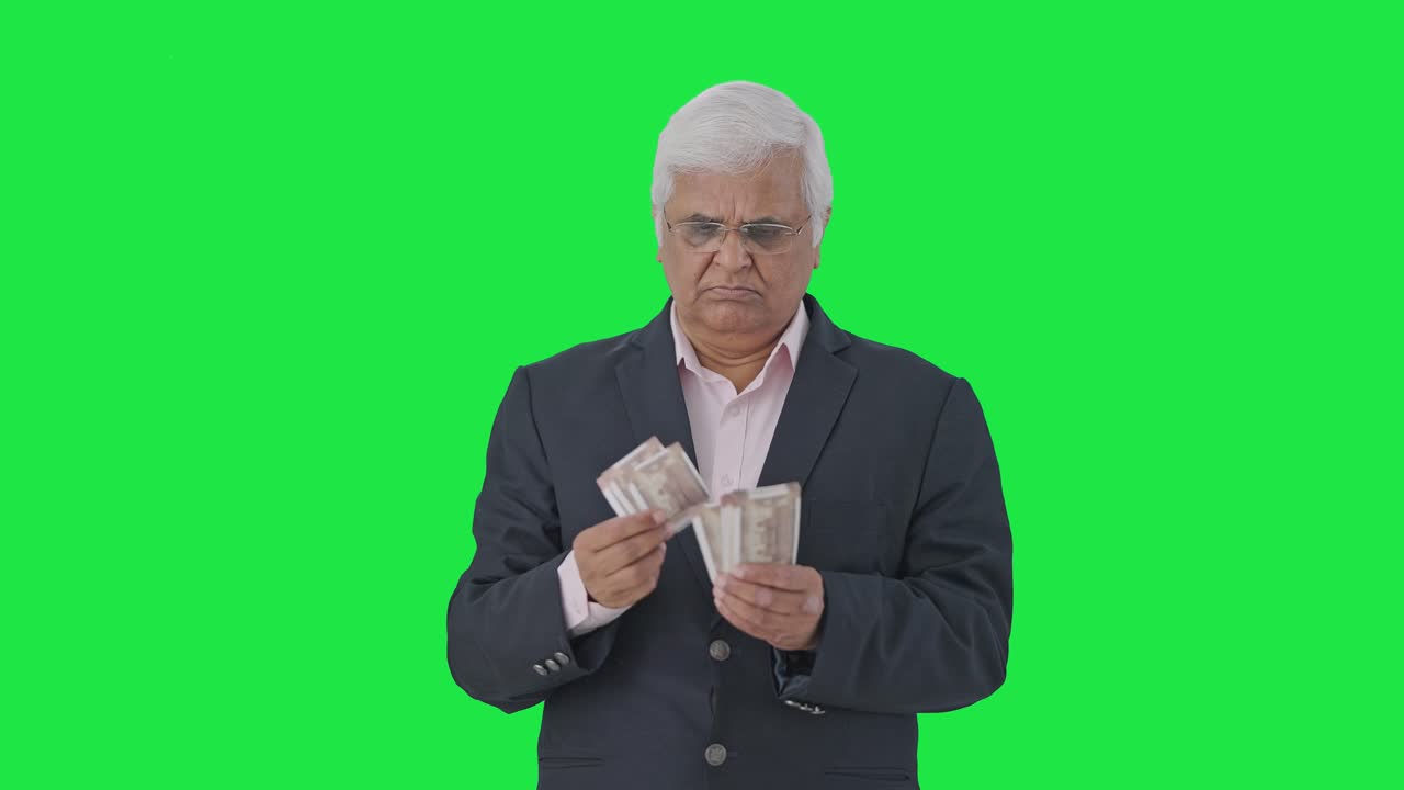 Tensed Indian senior manager counting money Green screen