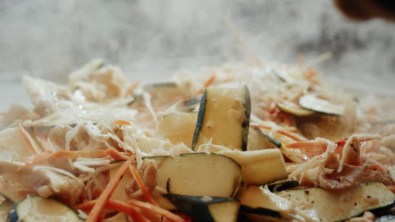 Chef with cooking gloves throwing more veggies into steaming wok dish