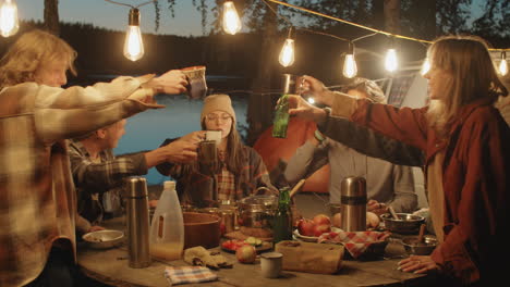 group of friends toasting with drinks at camping dinner