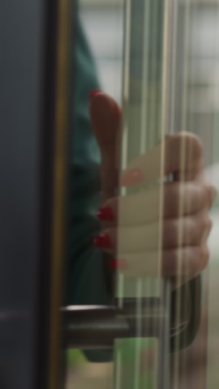 Woman puts hand on iron handle opening big glass door of modern office building. Glass door reflects stylish lady in green jacket an d city street slow motion