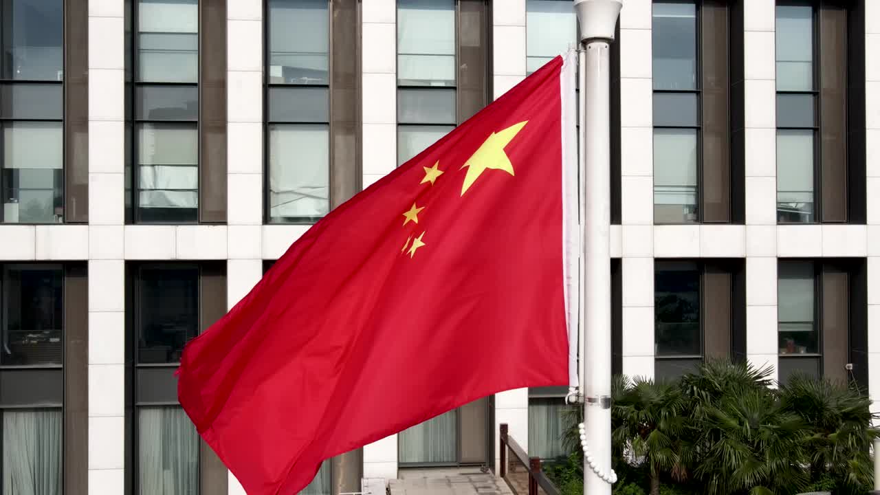 Bandeira Nacional Chinesa tremulando ao vento em frente a um edifício de escritórios moderno.