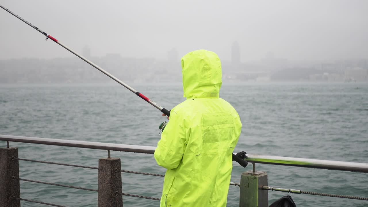 Fisherman in a yellow raincoat on a pier in a rainy day