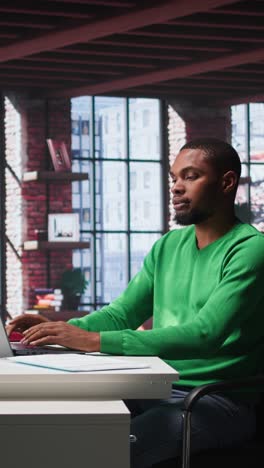 Vertical Video African american male teleworker completing spreadsheets on laptop
