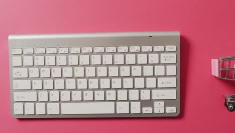 Overhead-view-of-computer-keyboard,-shopping-trolley-on-pink-background