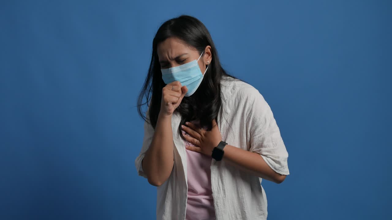 A young Asian woman wearing a medical mask on his face feeling sick with a coughing disease like flu, covid, coronavirus, bronchitis, or asthma allergy. A woman with an itchy and scratchy throat