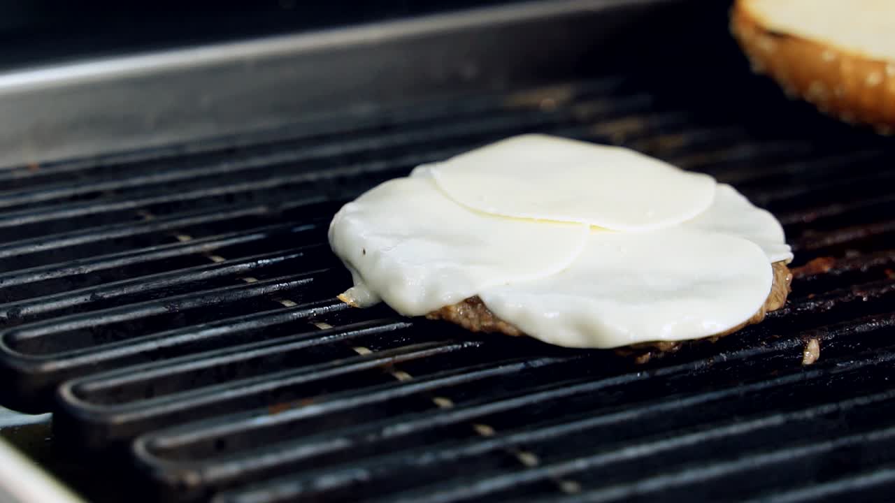 Melted cheese on cutlet for cheeseburger. Cooking delicious burger with meat and cheese on hot grill. Preparation of tasty hot sandwich in the restaurant