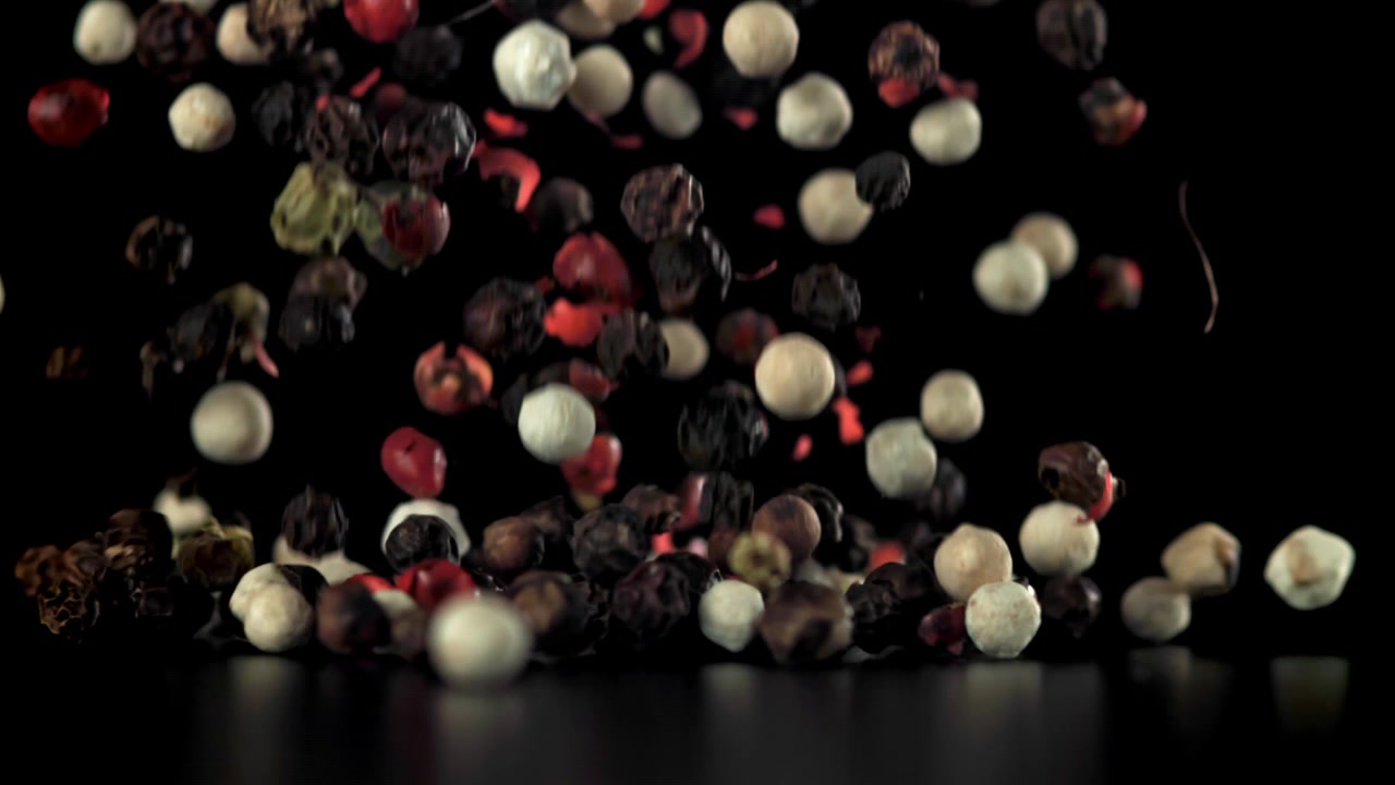 Mixed Peppercorns Falling in Slow Motion on Black Background