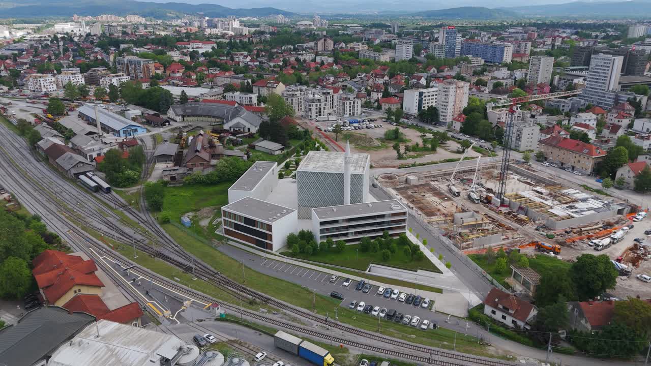 Aerial orbit over Islamic cultural centre of Ljubljana, Slovenia’s only mosque, modern architecture amid city skyline and active construction site.