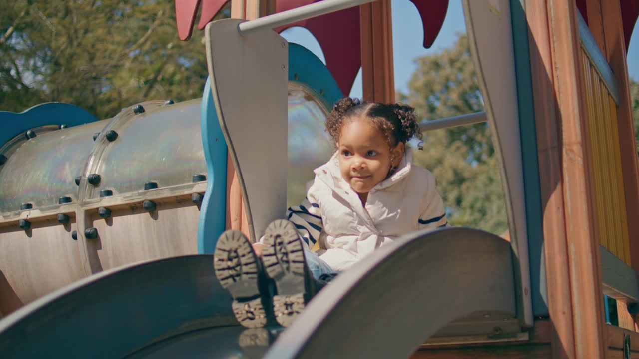 mujer juguetona deslizándose hija en el patio de recreo de cerca. la familia se divierte