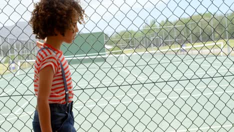 Side-view-of-mixed-race-schoolgirl-walking-near-wire-mesh-fence-at-school-4k