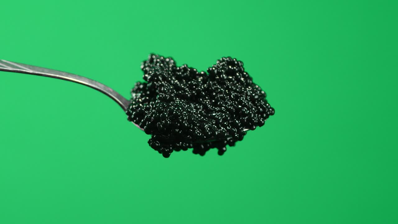 The man's hand holds a spoon with black caviar.