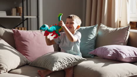 a young child happily plays with a colorful dinosaur toy on a sofa